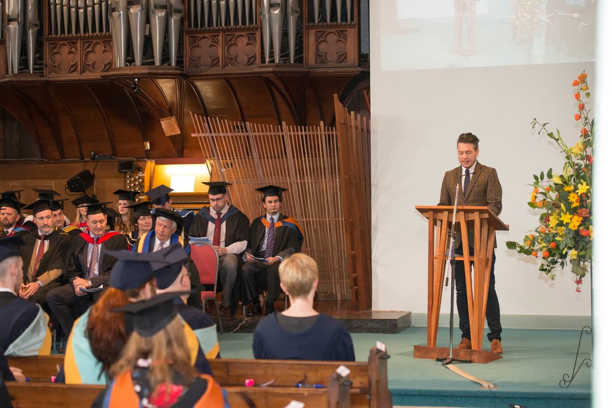Wide shot of Shane presenting to a large conference audience with professional AV setup