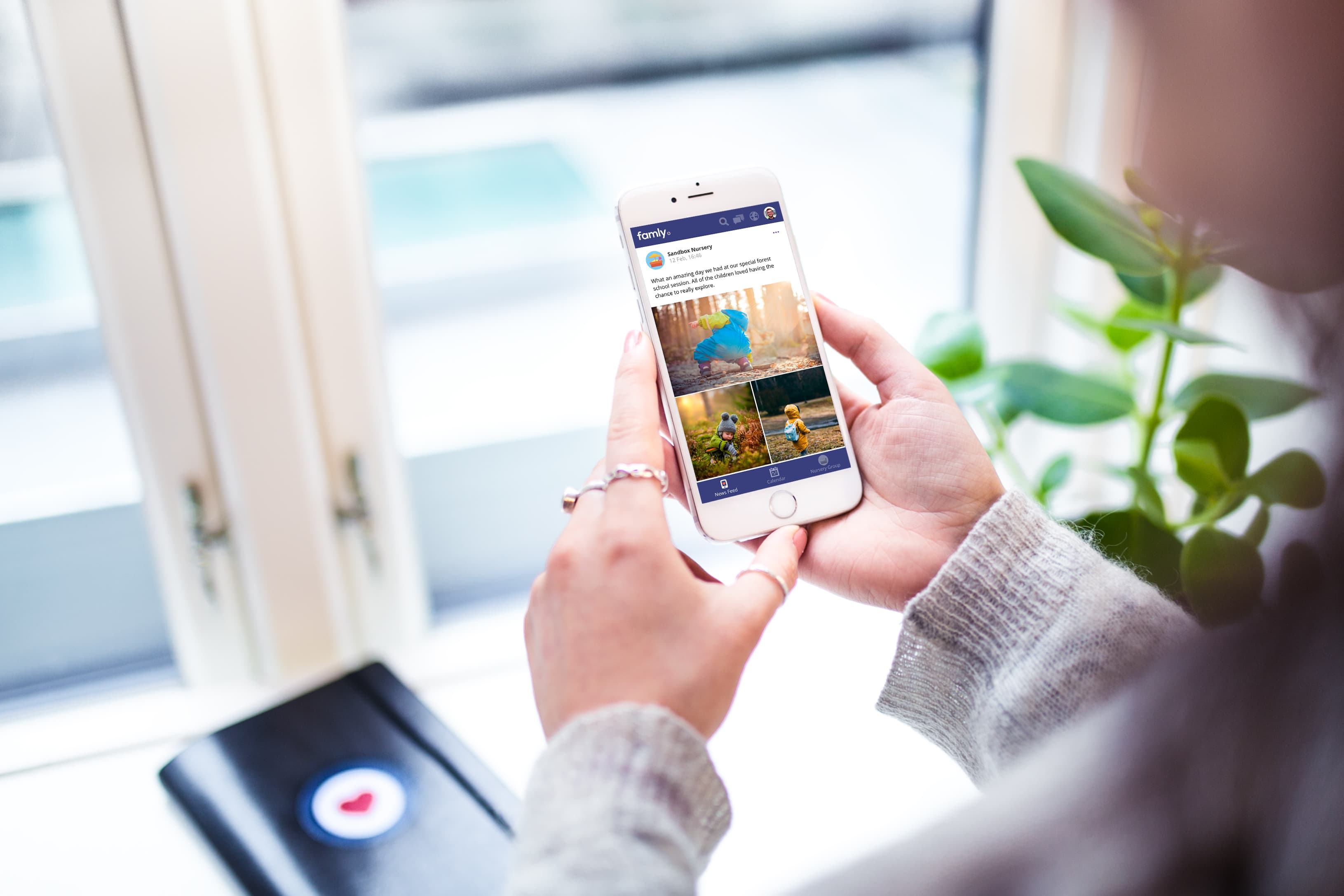 The Famly newsfeed on a phone, held in someone's hands by a window